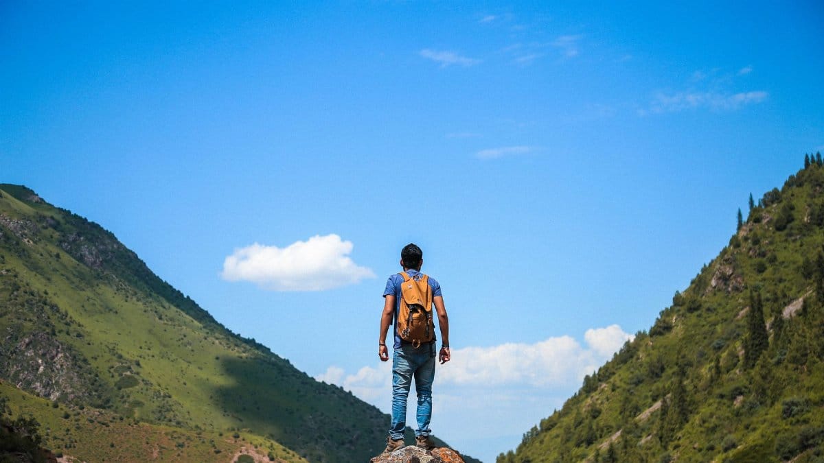A solo backpacker standing on a rock, admiring the mountain view under a bright blue sky.