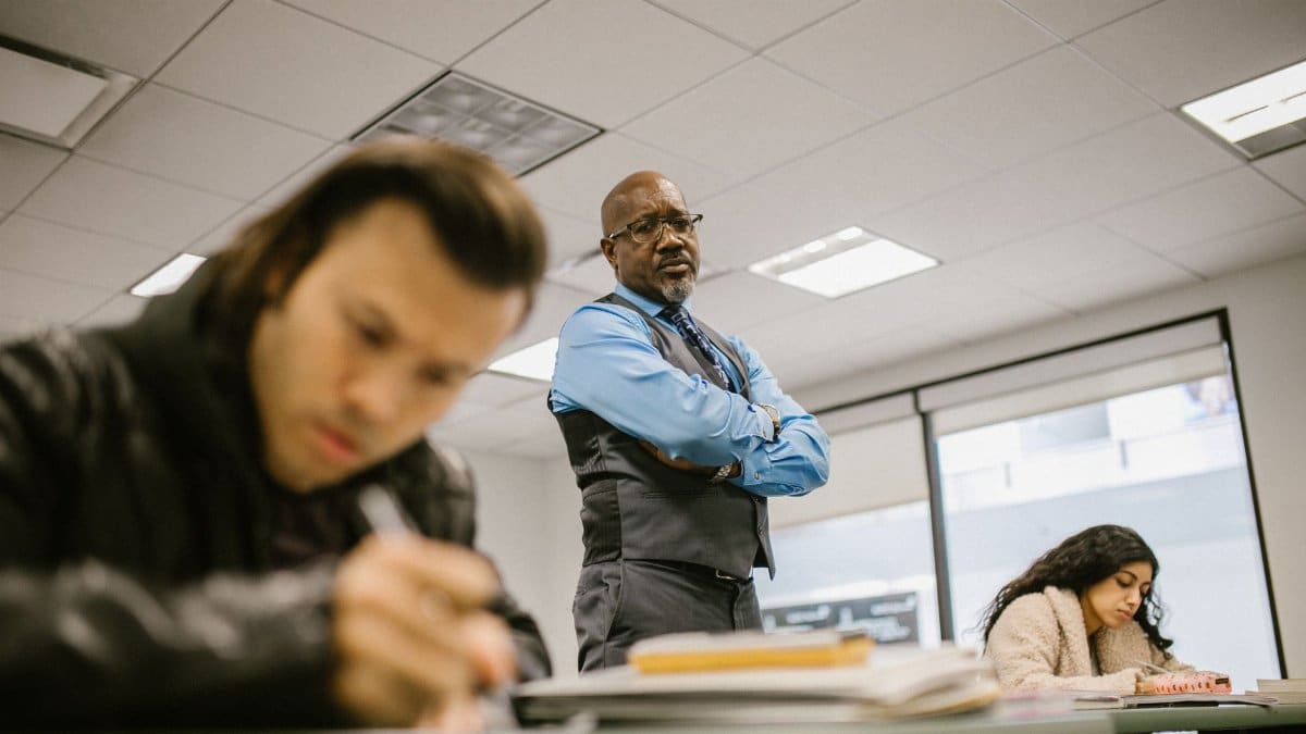 A professor supervises students during an exam, ensuring integrity in a classroom setting.