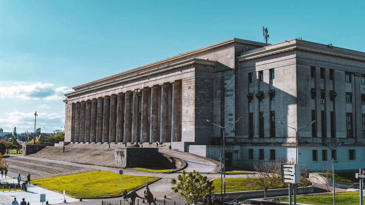Exterior view of a historic university building with columns in Buenos Aires, Argentina. Clear sky and people present.