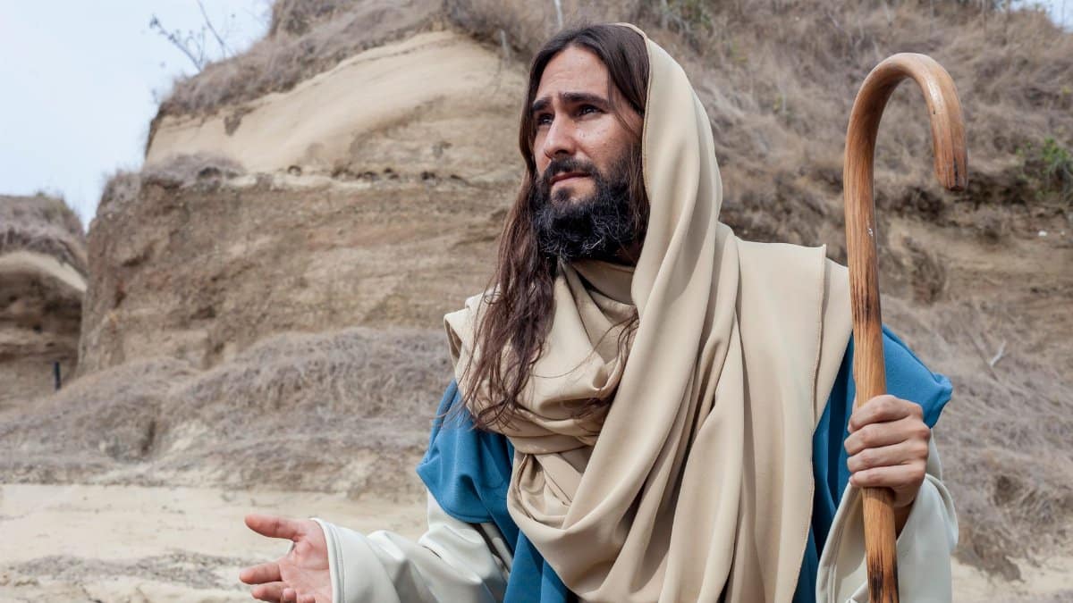 A man dressed as a biblical shepherd with crook in a rustic Colombian landscape.