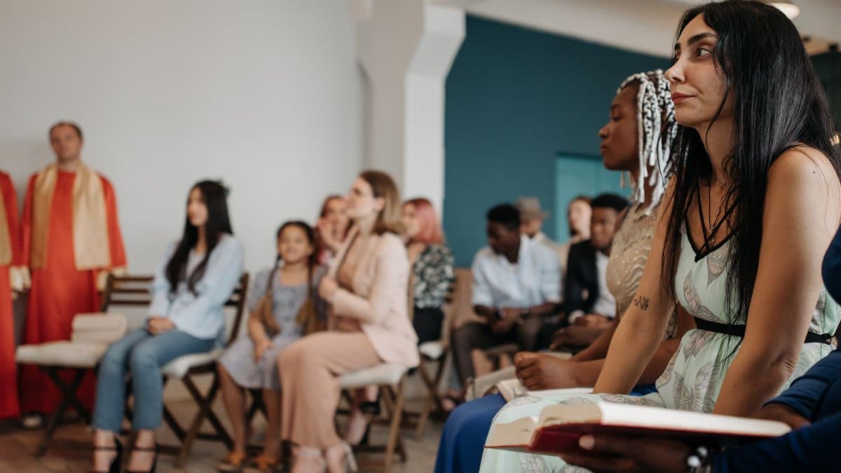 A multi-ethnic group of people attentively listening during a religious gathering indoors.