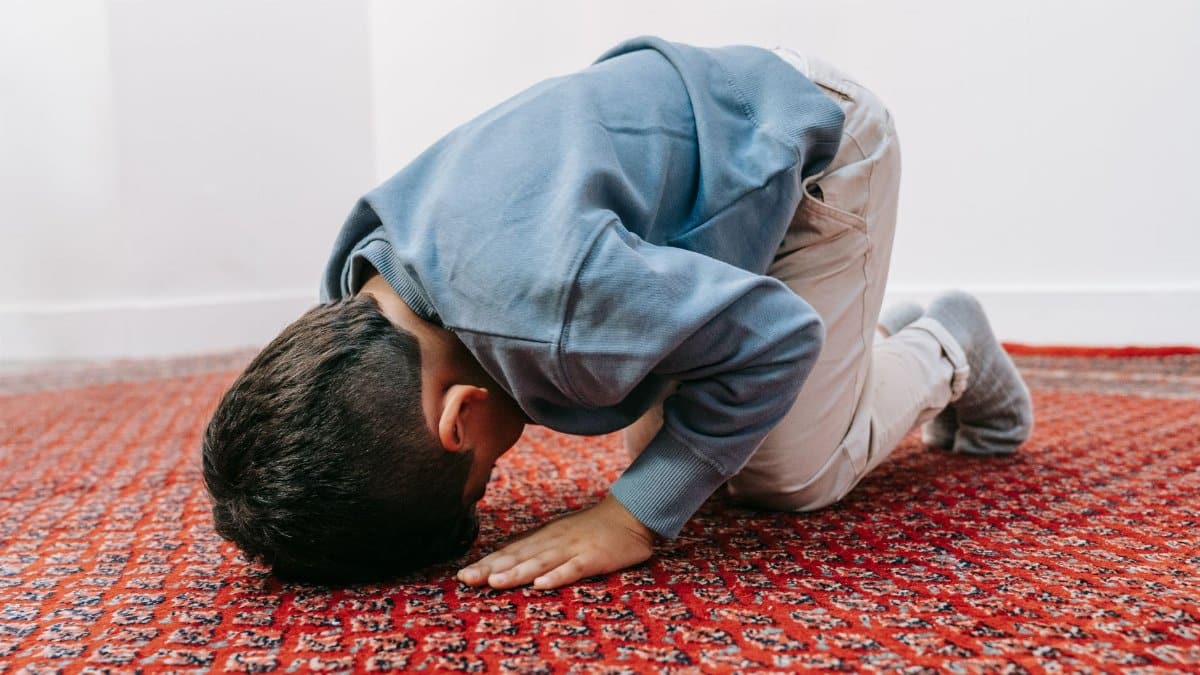 A child kneels and prays indoors on a red patterned rug, embodying devotion and tranquility.
