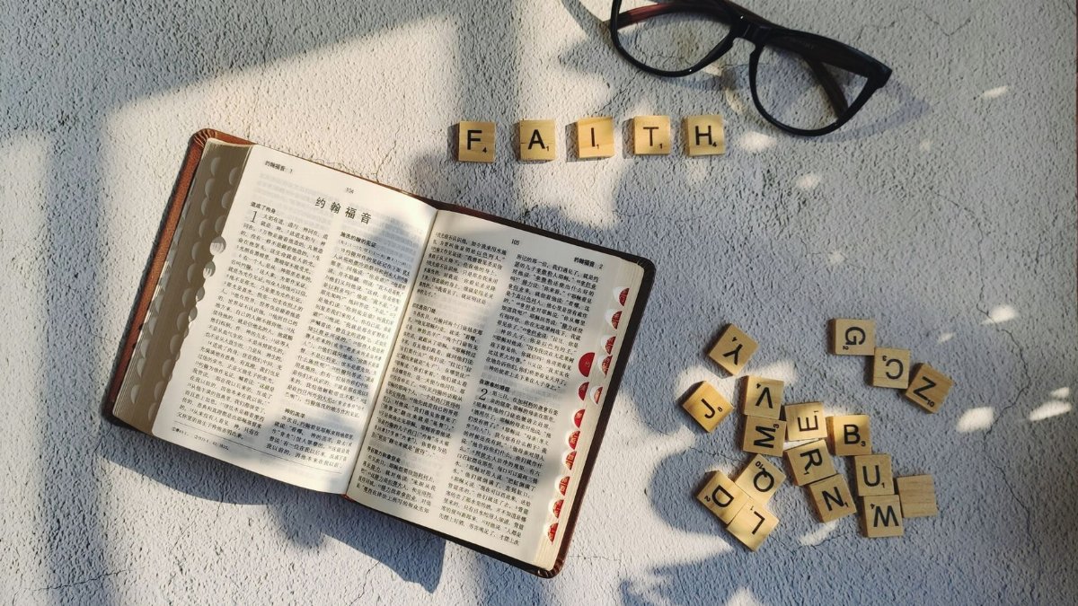 An open Bible in Chinese with letter blocks spelling 'faith' and eyeglasses on a textured surface.