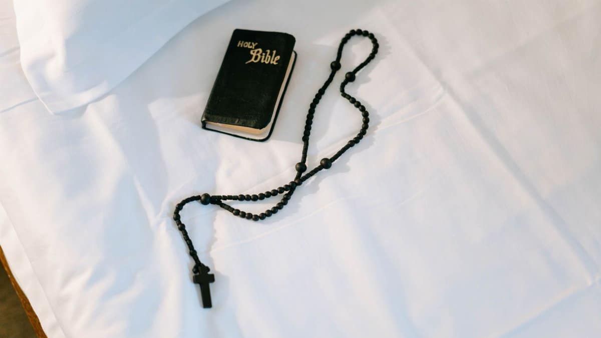 A top-down view of a Holy Bible and rosary on a white cloth, symbolizing faith and devotion.