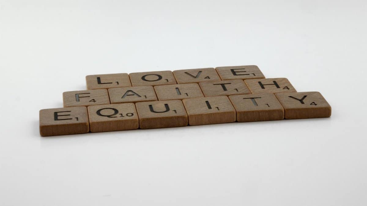 Wooden scrabble tiles on white surface spelling love, faith, and equity.