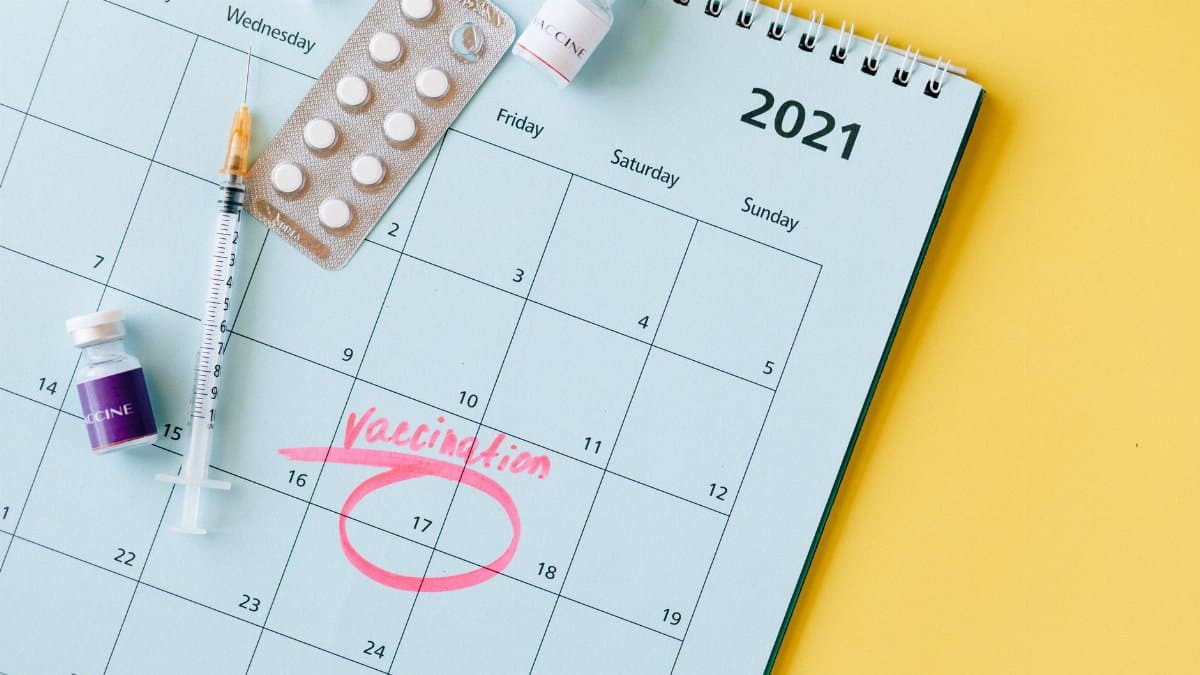 Calendar with vaccination date circled alongside vaccine vials and syringe for COVID-19 prevention.