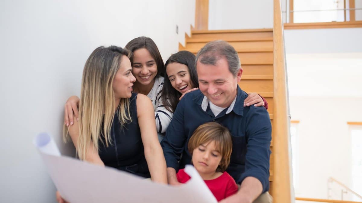 A joyful family gathers on a staircase, reviewing building plans indoors.