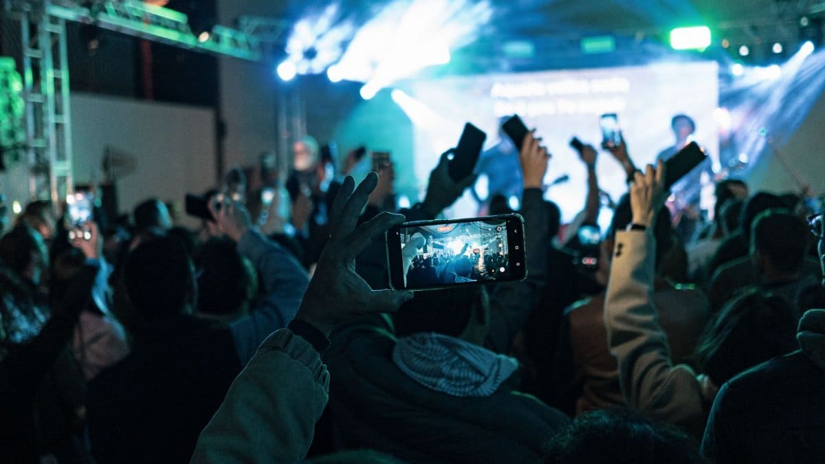 Lively crowd capturing concert moments on smartphones, vibrant lights create dynamic atmosphere.