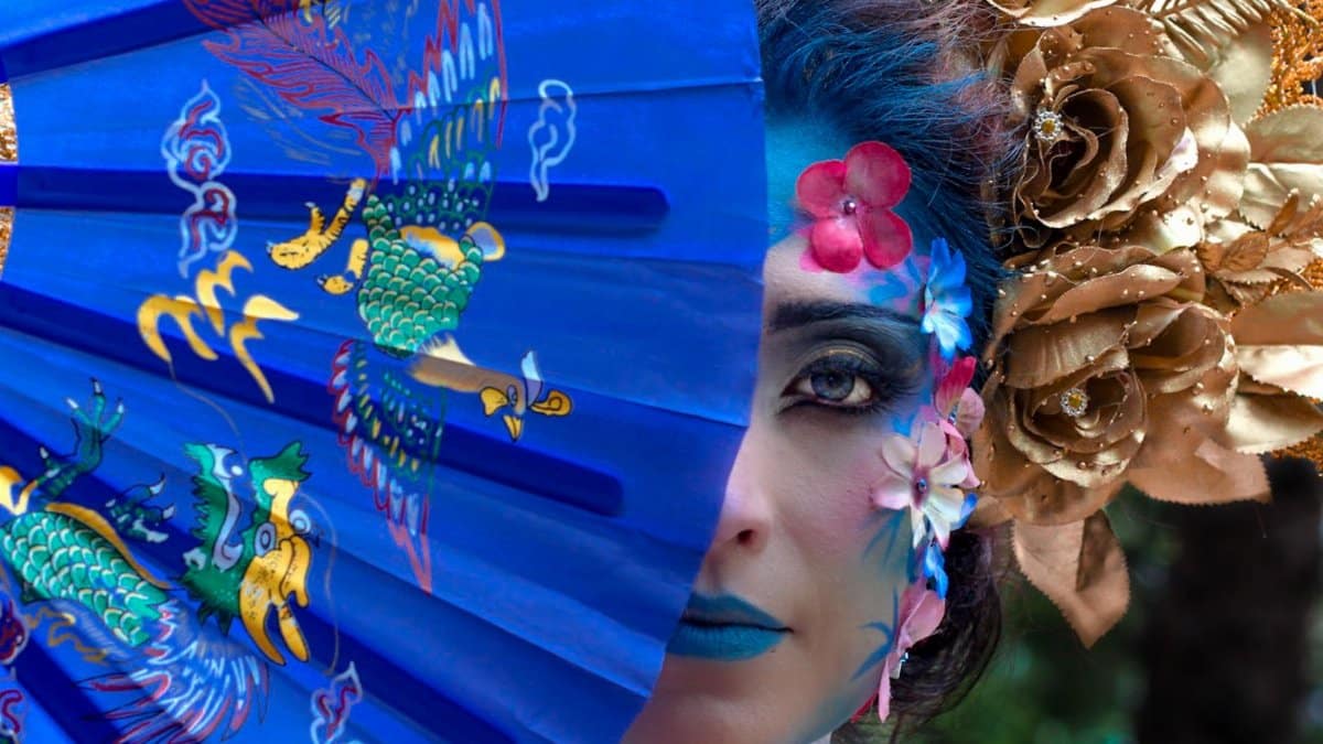Artistic portrait featuring a woman with blue fan, floral designs, and gold headdress in vibrant colors.