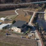 Aerial perspective of rural farmland featuring solar panels, fields, and a river.