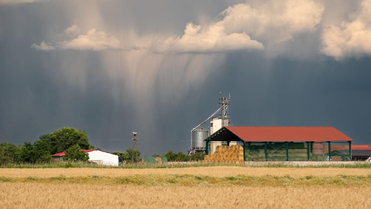 A countryside farm with dramatic storm clouds looming overhead, hinting at incoming rain.