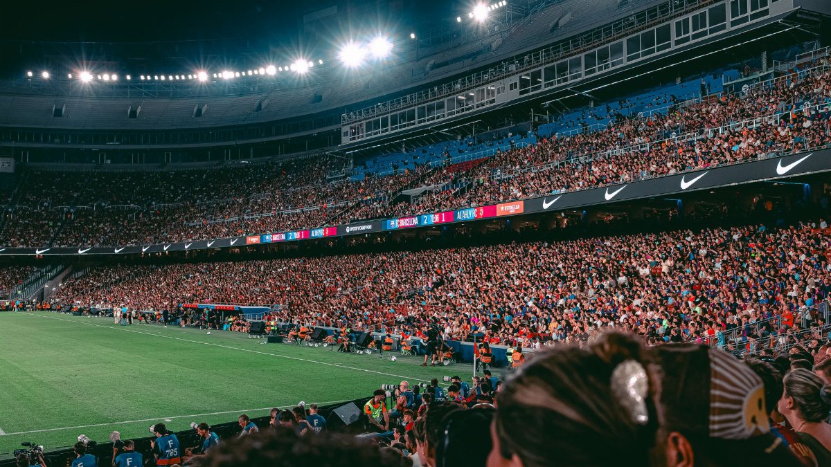 Packed football stadium under night lights with a cheering crowd and green field.
