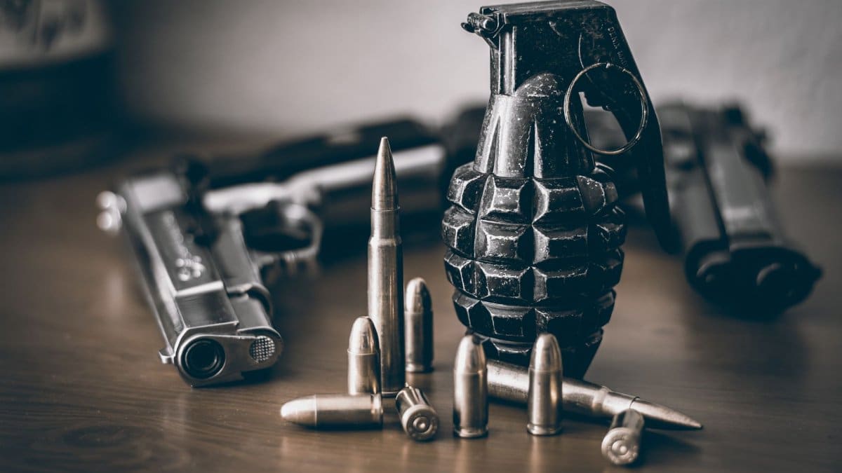 A collection of weapons including a pistol, grenade, and bullets on a wooden surface.