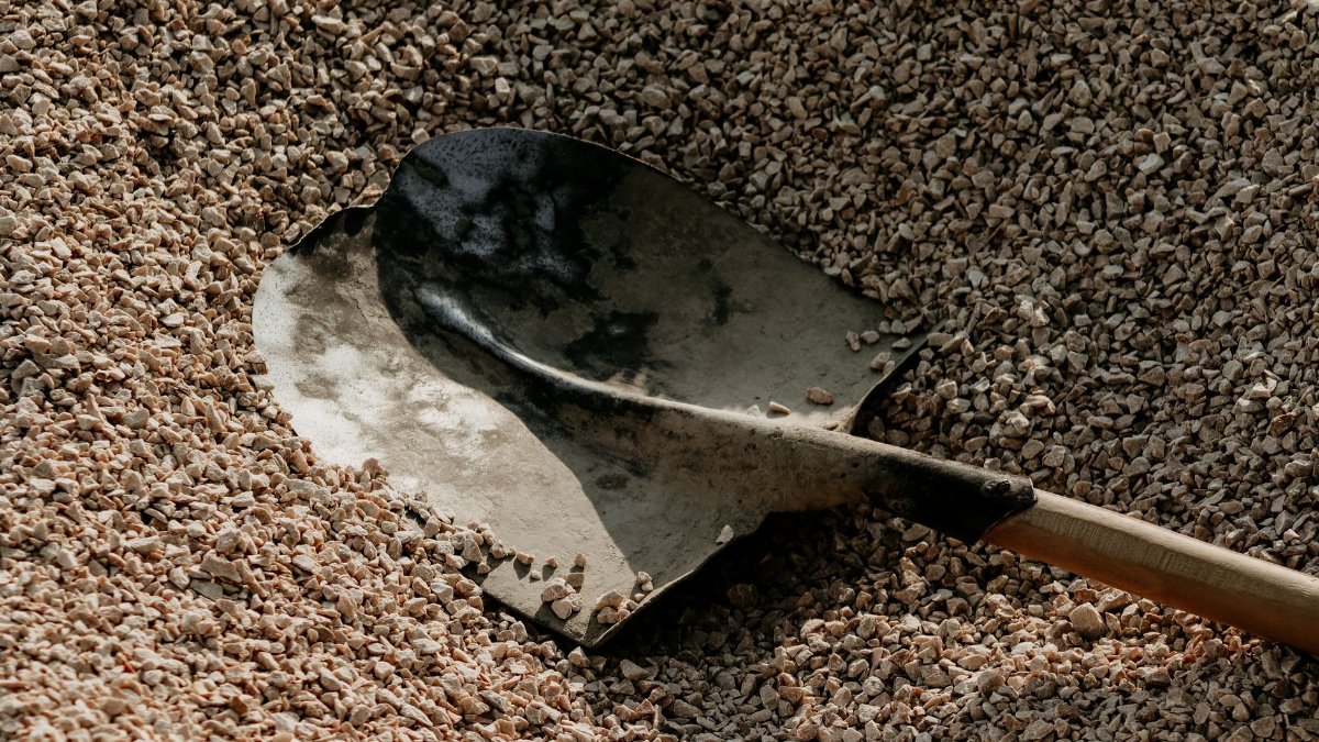A metal shovel lying on a pile of small pebbles, suggesting outdoor landscaping or construction activities.