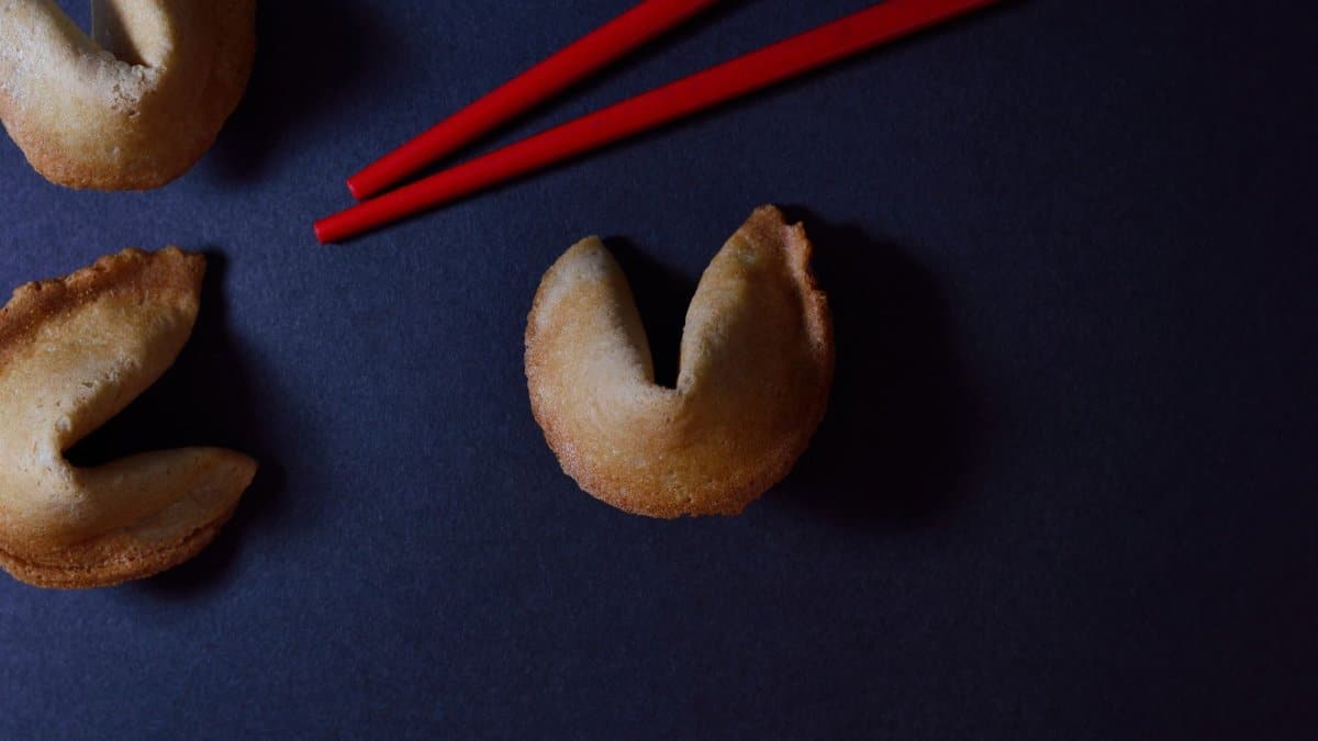 Close-up of fortune cookies next to red chopsticks on a dark background, creating a minimalist and stylish composition.