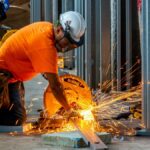 Workers cutting metal beams with a grinder, creating sparks inside a construction site.