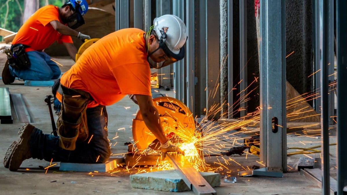 Workers cutting metal beams with a grinder, creating sparks inside a construction site.
