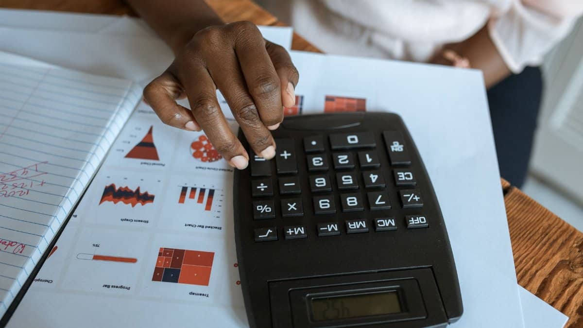 Person using calculator on desk with financial charts and graphs, ideal for business and finance themes.