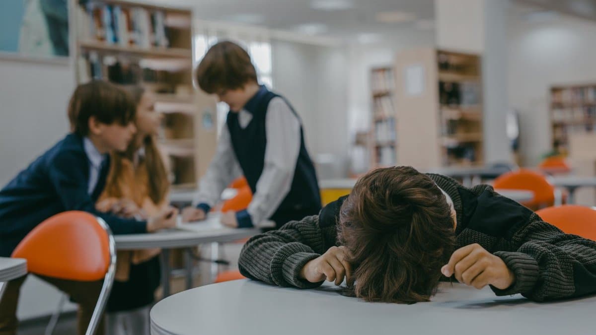 A child sits alone in a school library, highlighting themes of bullying and isolation.