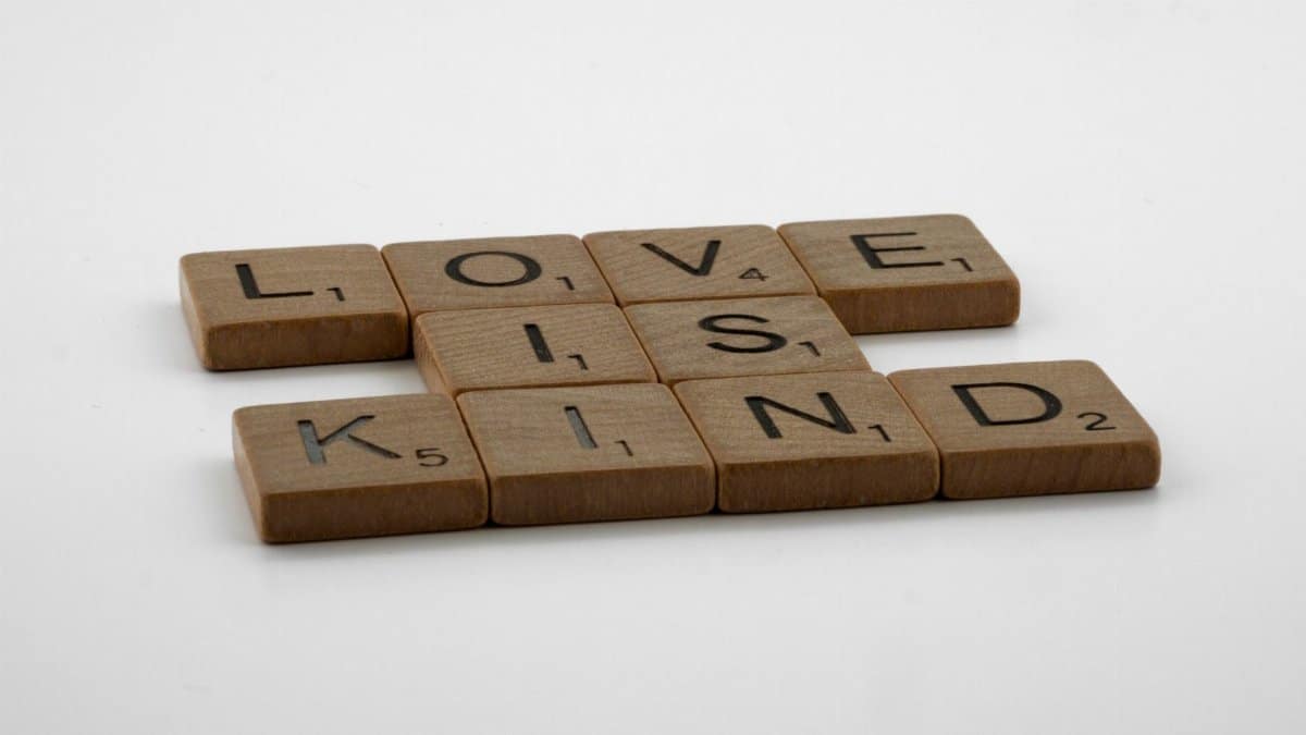 Wooden Scrabble tiles arranged to say 'Love is Kind' on a plain background.