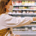 Woman wearing a face mask while selecting fruit in a supermarket, highlighting safety measures.