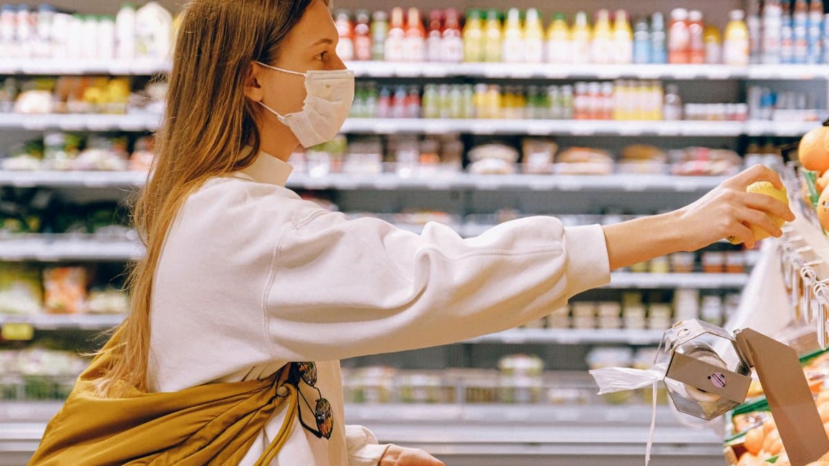 Woman wearing a face mask while selecting fruit in a supermarket, highlighting safety measures.