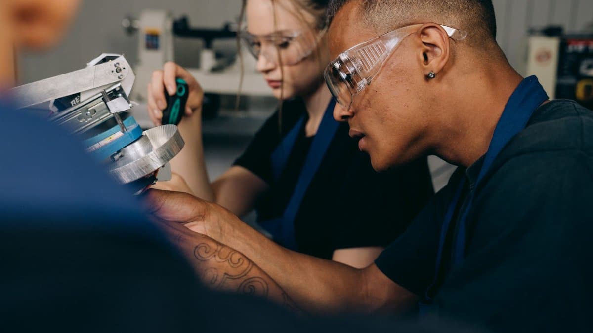 Two young adults working attentively in a workshop, wearing protective goggles.