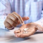 Close-up of a man's hands holding and pointing at white pills next to a prescription bottle.