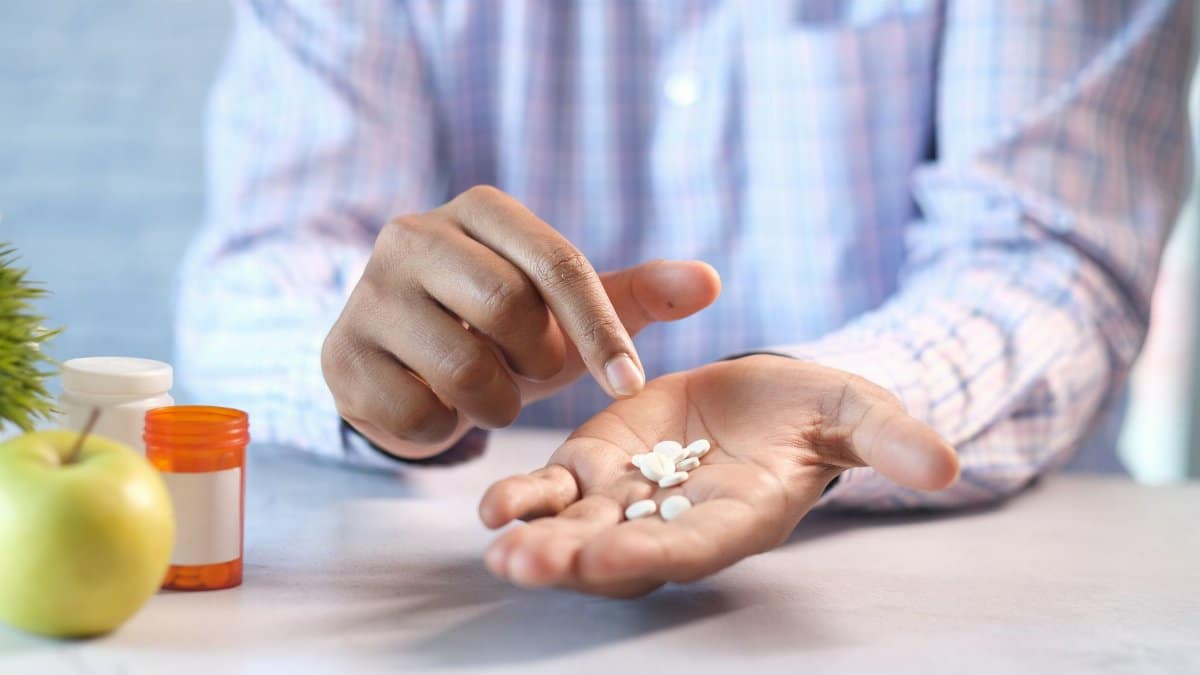 Close-up of a man's hands holding and pointing at white pills next to a prescription bottle.