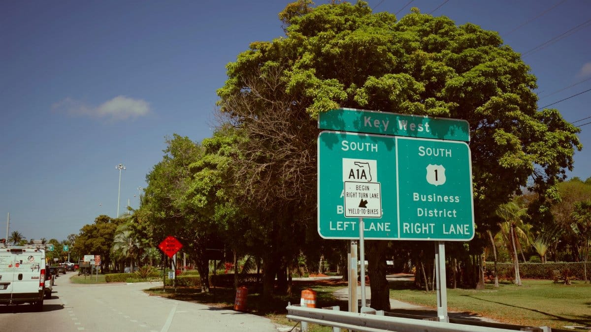 Directional sign for Key West, Florida on a clear day. Green road signs guide travelers southwards.