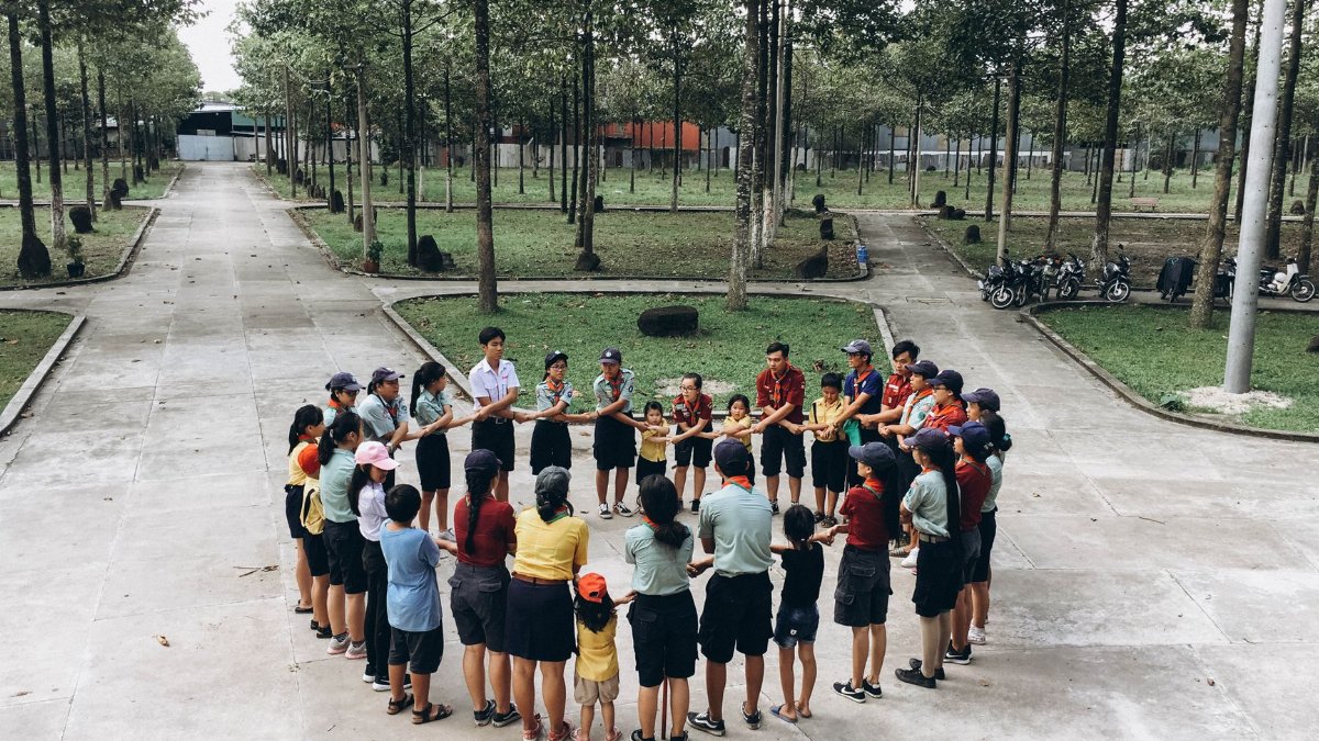 Group of people engaging in a team-building exercise outdoors, forming a circle in a park setting.