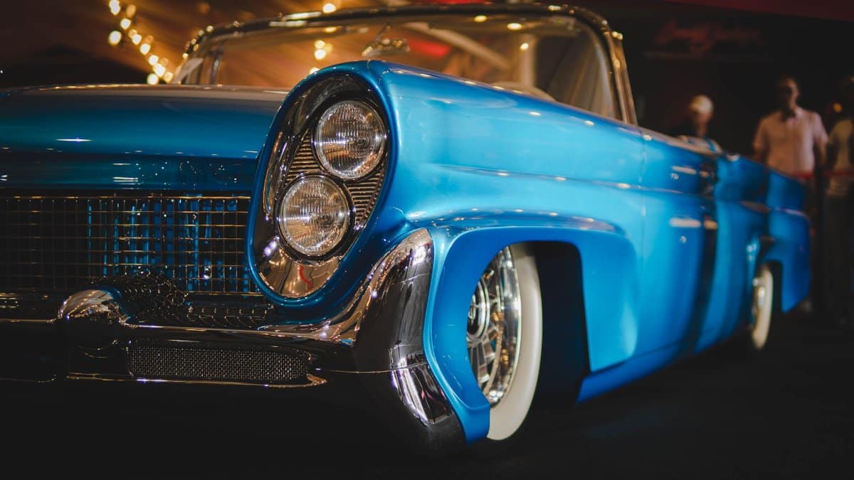 Detailed image of a vintage blue convertible car with chrome accents at a car show.