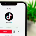 Close-up view of hand holding smartphone displaying TikTok app interface with profile page.