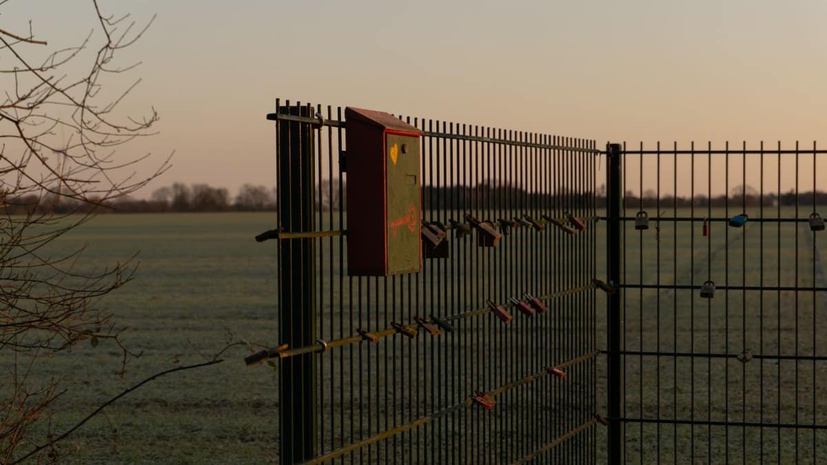 A scenic view of love padlocks attached to a fence with a mailbox, capturing the serene sunrise in Achim, Germany.
