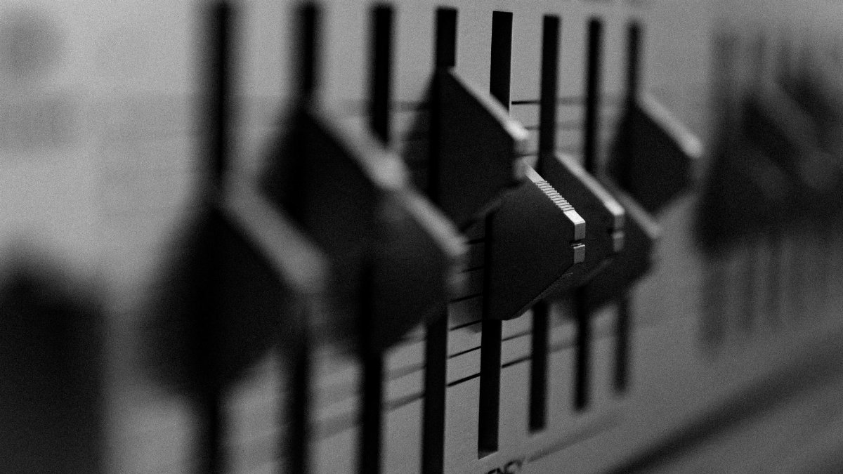 Black and white close-up of an audio mixer showing adjustment knobs and frequency settings.