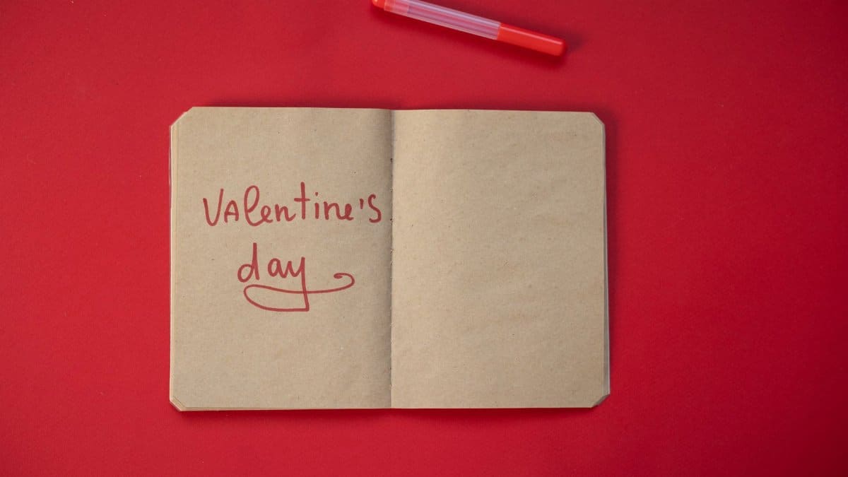 Top view of Valentines Day phrase written in notebook with craft paper placed on red background with felt pen during holiday