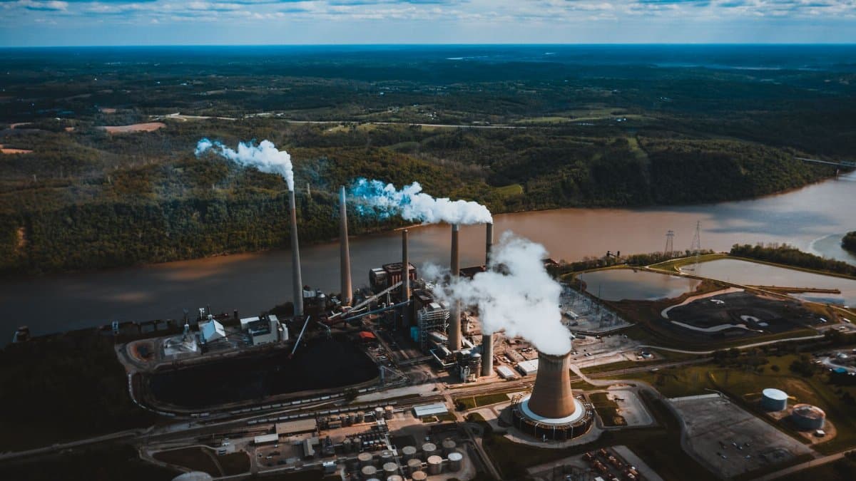 Aerial view of industrial landscape of city with smoke emissions from chimneys located near river and forest