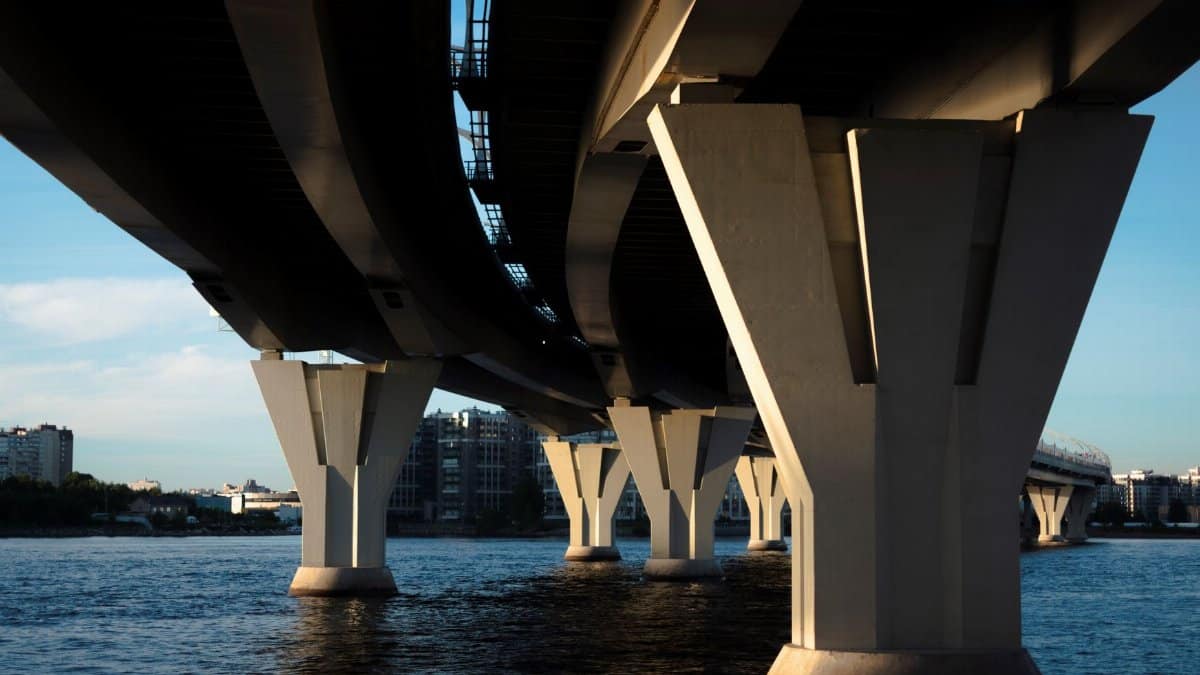 A striking view of a modern bridge understructure over a city waterfront at sunset, showcasing architectural design.