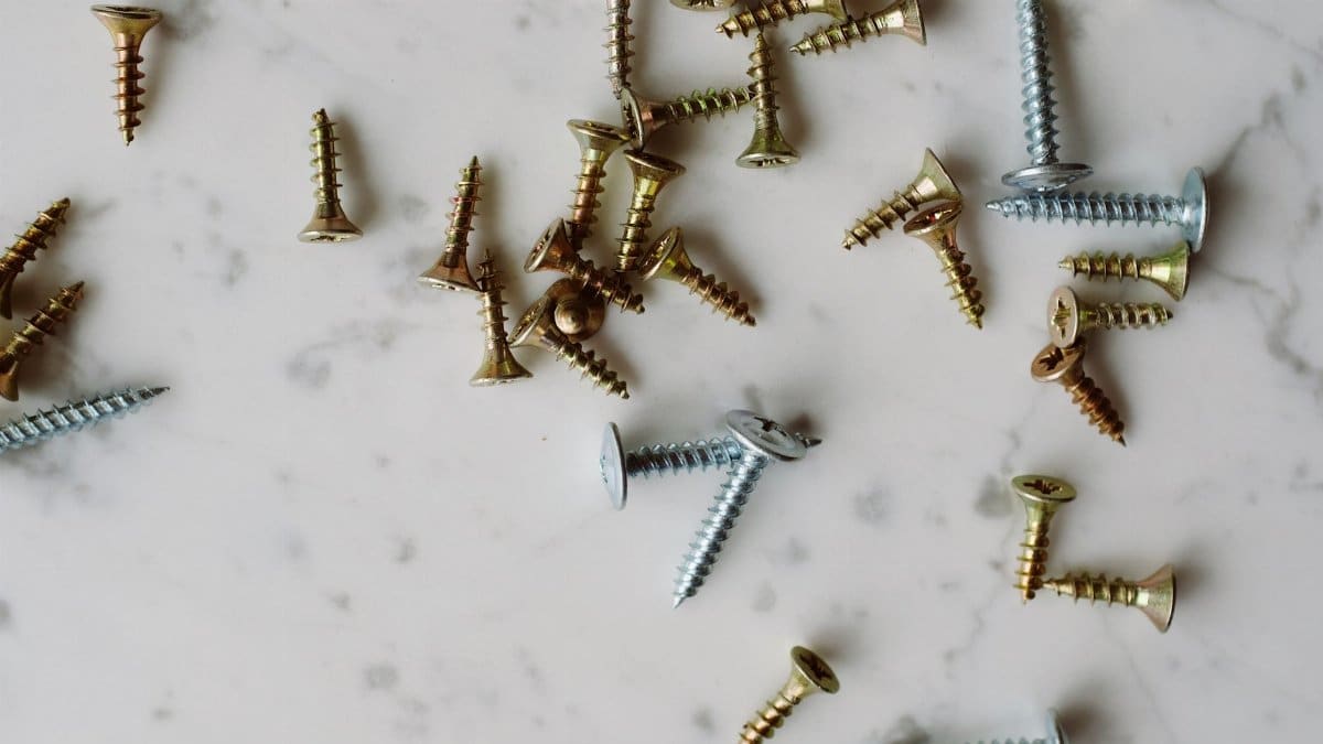 Set of various metal screws of different sizes placed on white marble table in modern workshop