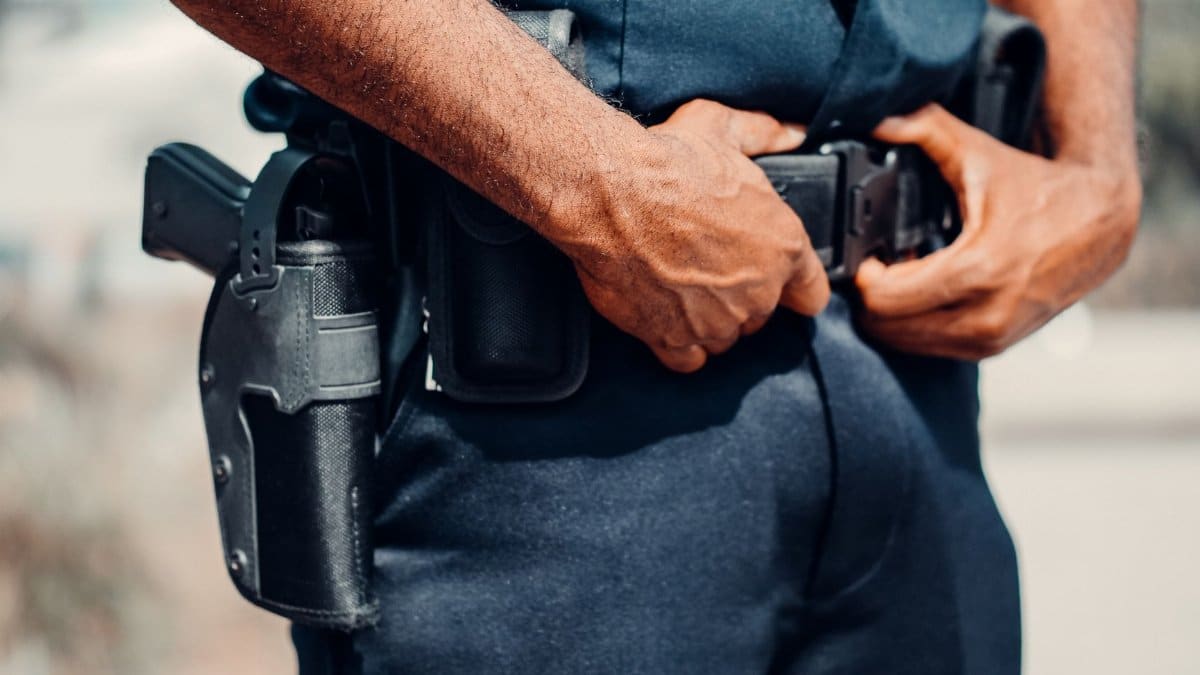 A police officer adjusts their utility belt outdoors, showcasing law enforcement gear and uniform.