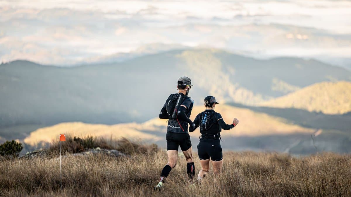 Two trail runners navigate a scenic mountain landscape during daylight hours.
