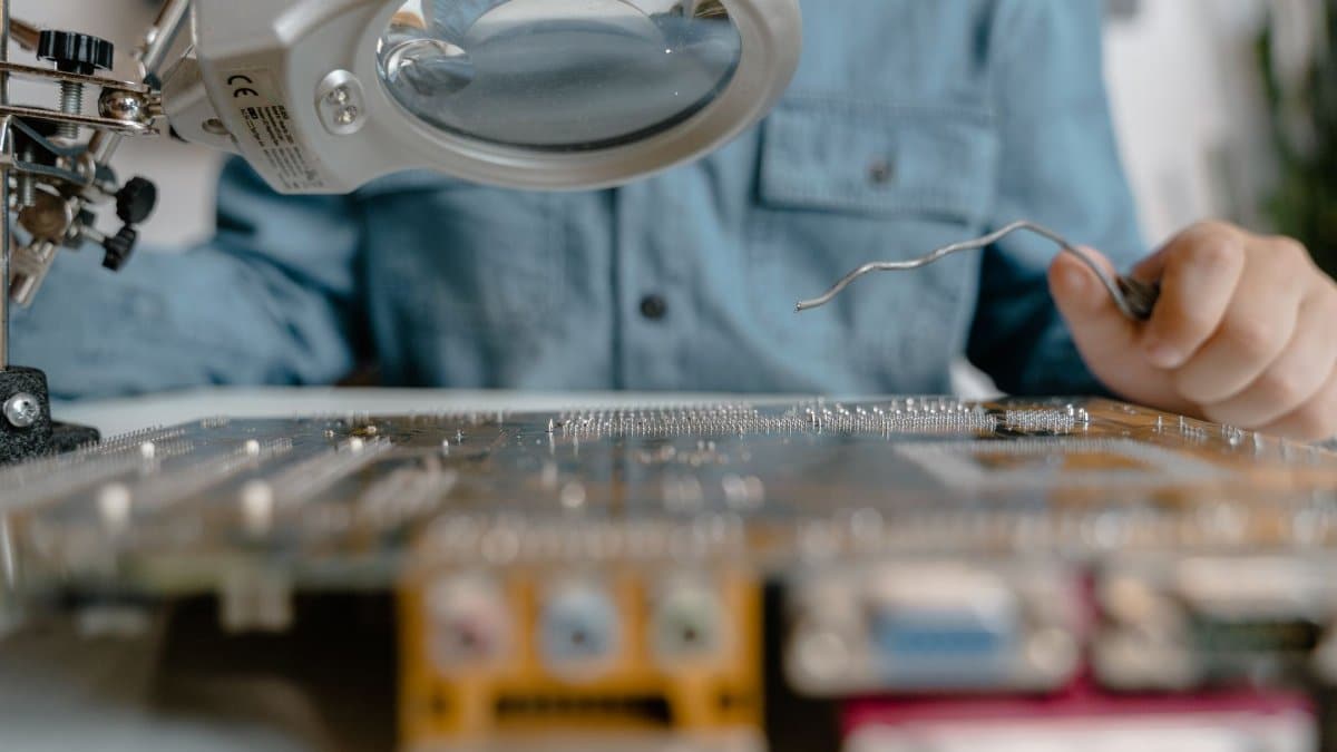 A detailed view of electronic circuit inspection using a magnifying glass and tools.