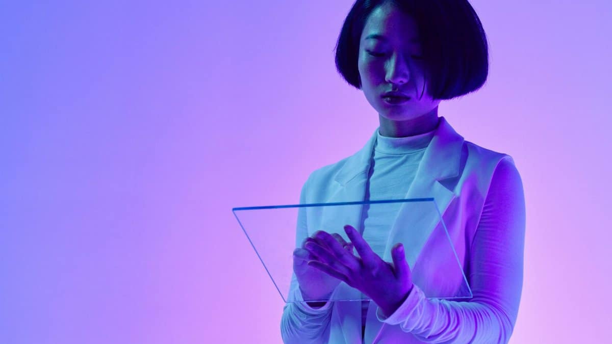 Woman interacts with a transparent digital screen in vibrant studio lighting.