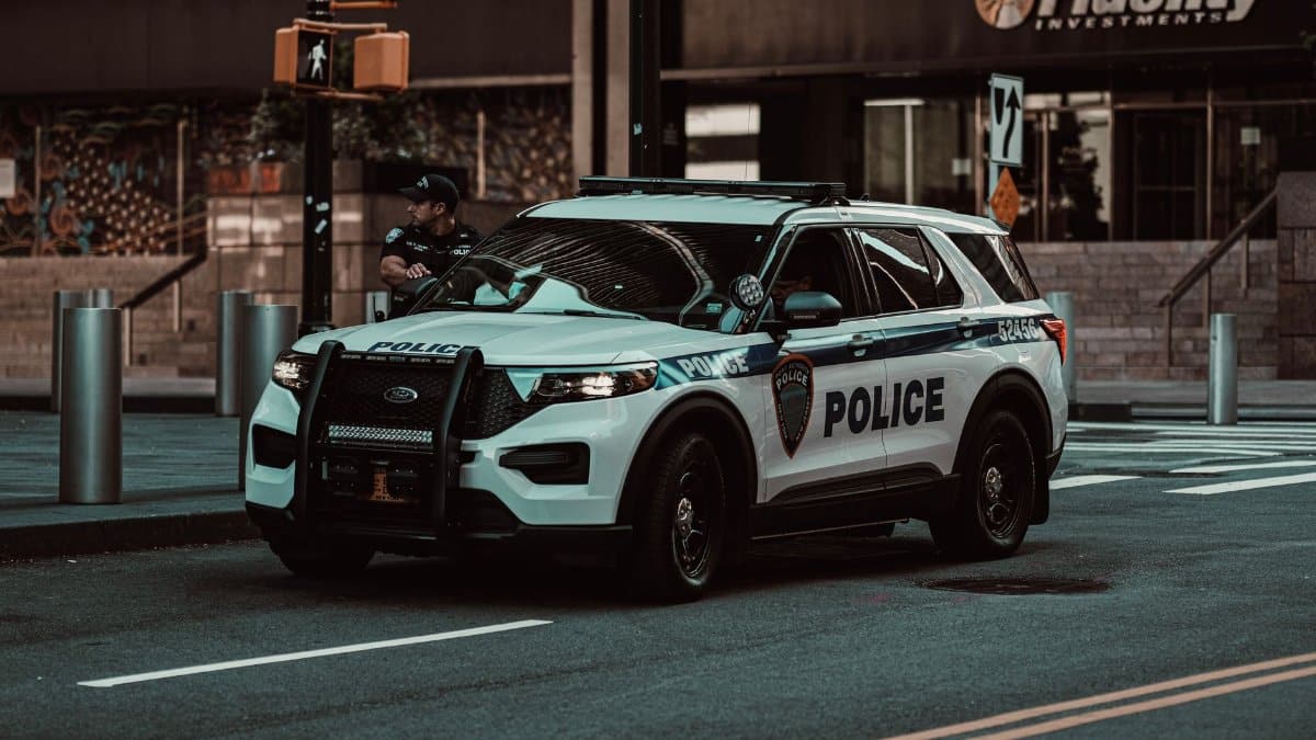 A police car parked on a street in New York City with a policeman nearby, showcasing urban safety.