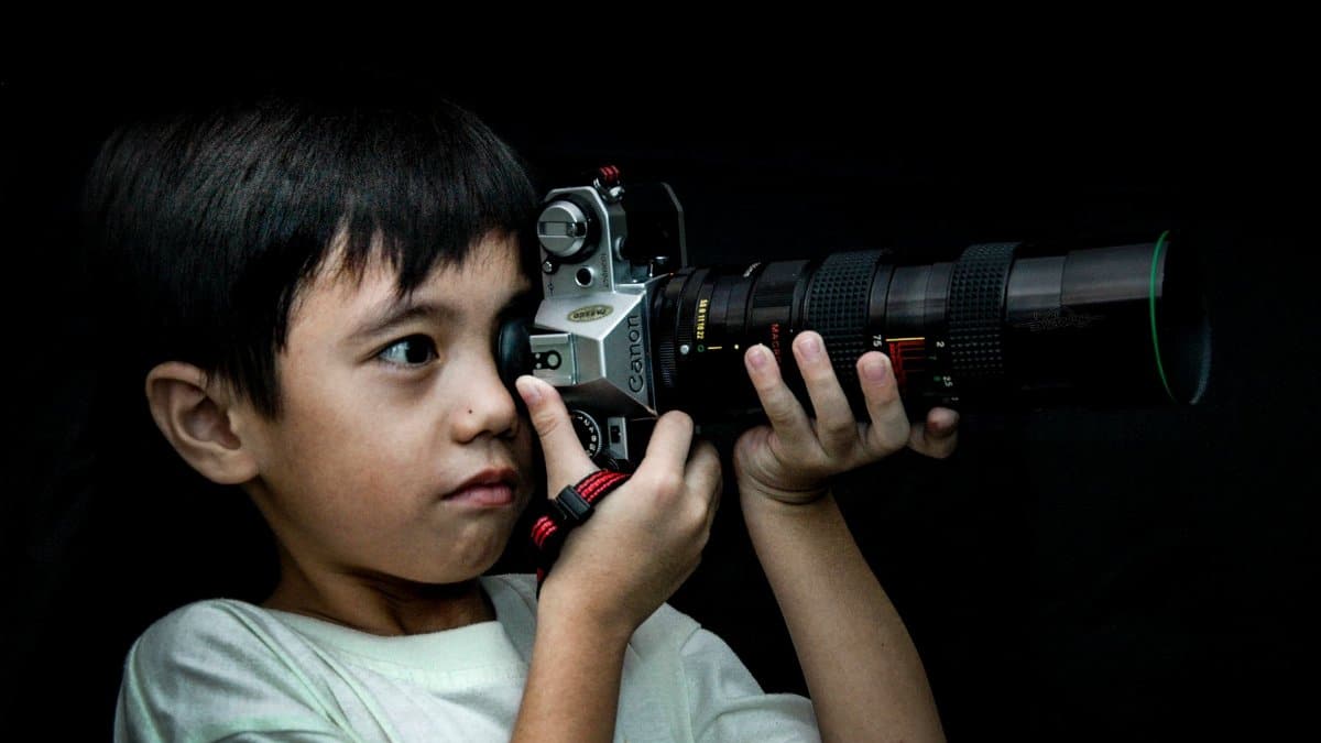 A child enthusiastically looks through a camera viewfinder, capturing the essence of budding creativity.