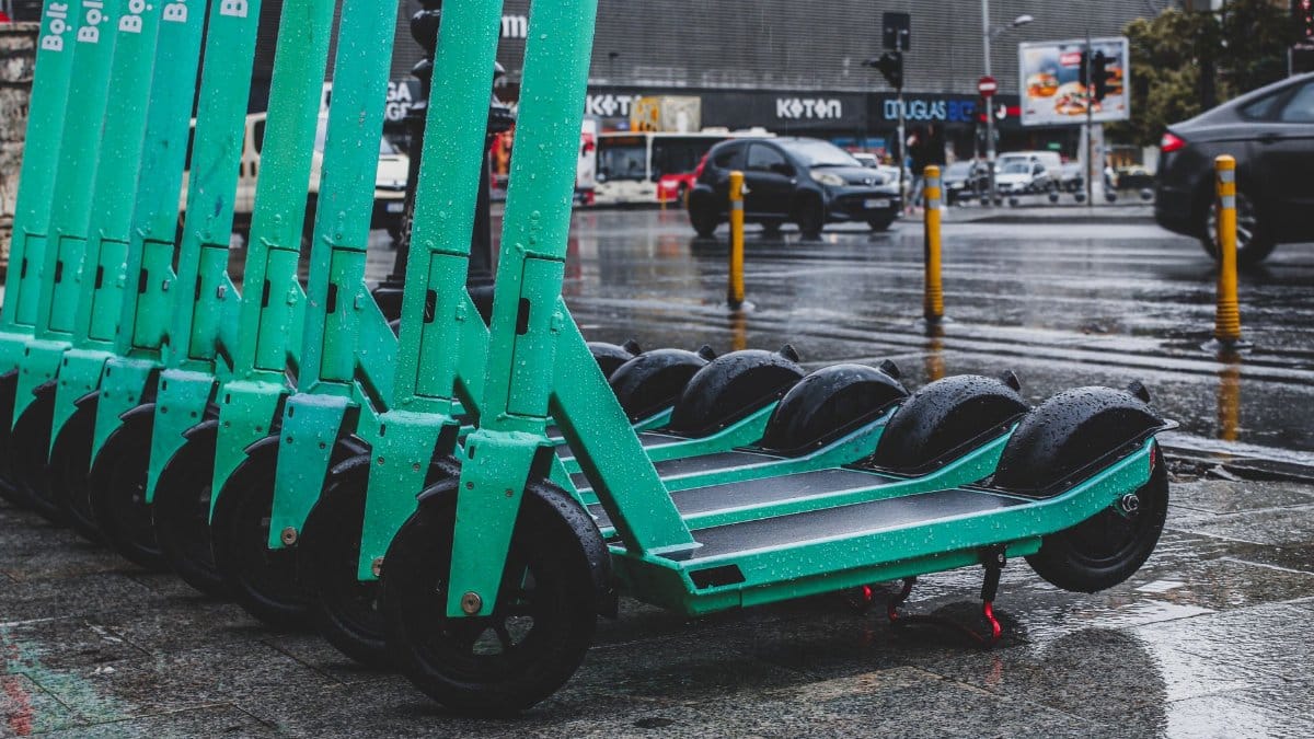 Rain-soaked electric scooters lined up on a city street, reflecting urban transportation.