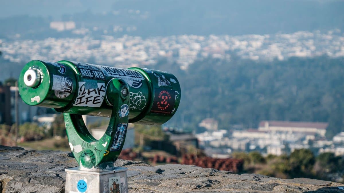 Green public binoculars overlooking a cityscape, offering a scenic urban view.