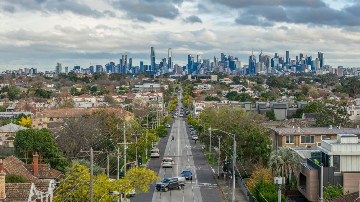 An expansive view of Melbourne's suburban road leading to the city skyline with lush greenery and overcast skies.
