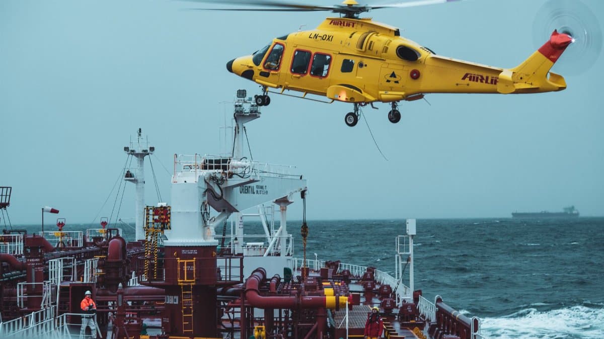 A yellow rescue helicopter hovers over a cargo ship in turbulent waters, highlighting maritime rescue operations.