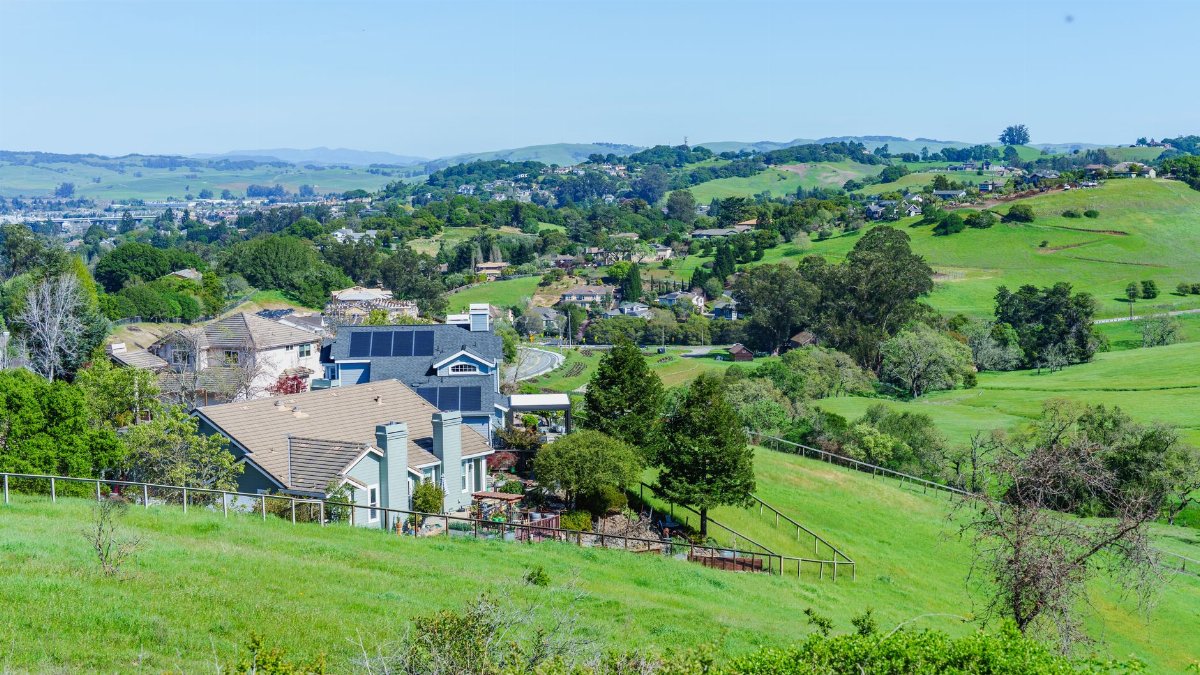Picturesque suburban neighborhood with lush green hills and clear blue skies, showcasing a peaceful, idyllic lifestyle.